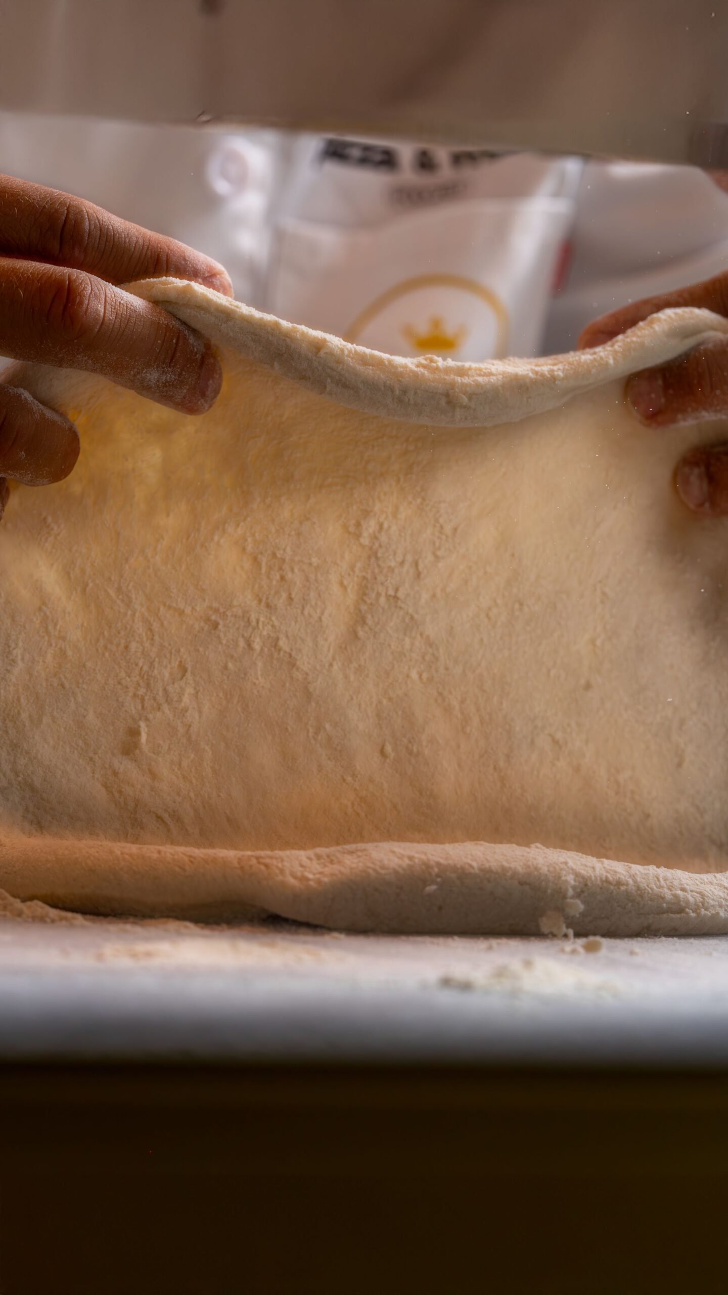 Hands Stretching Fresh Pizza Dough in Kitchen