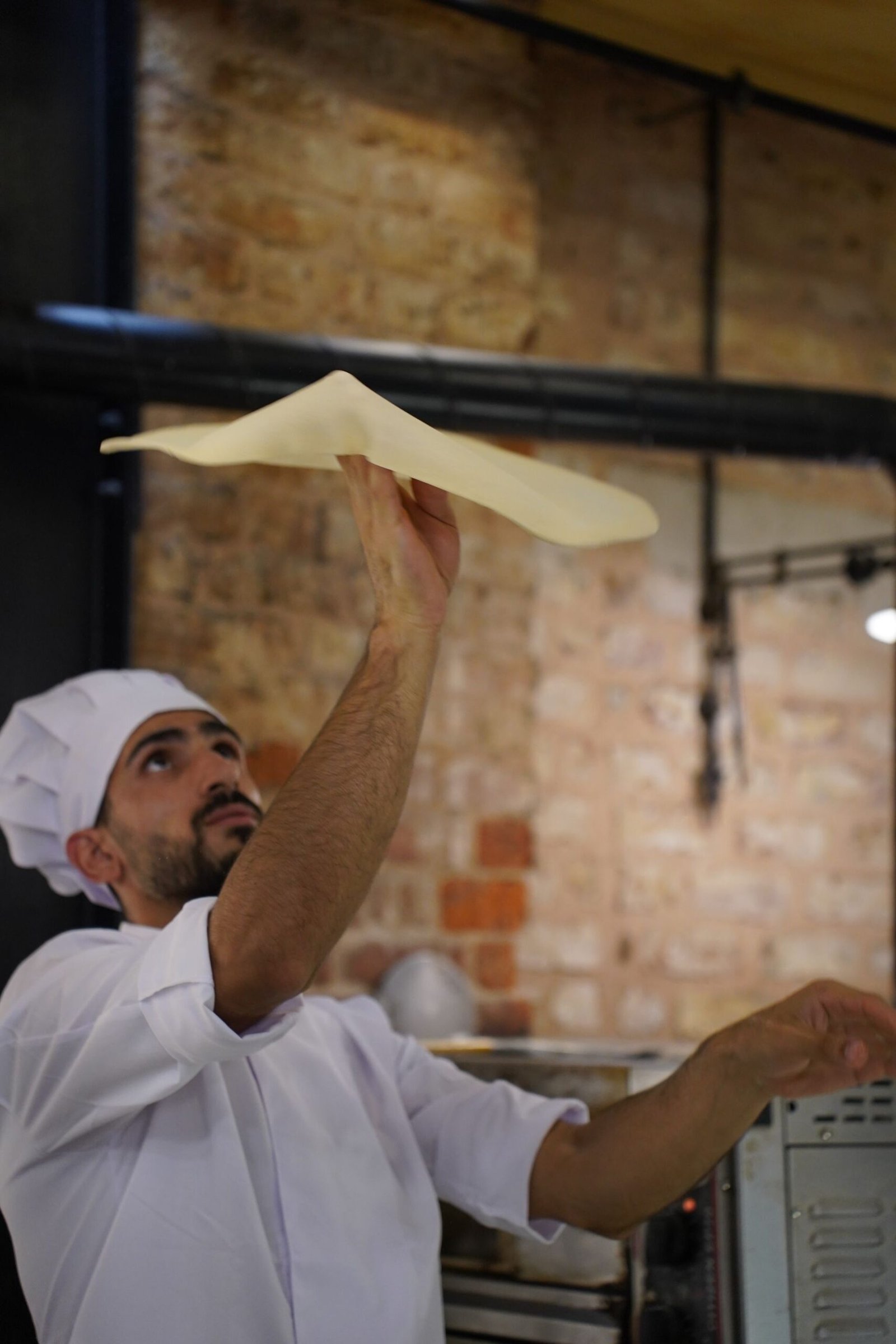 Chef Tossing Pizza Dough in Rustic Kitchen Setting