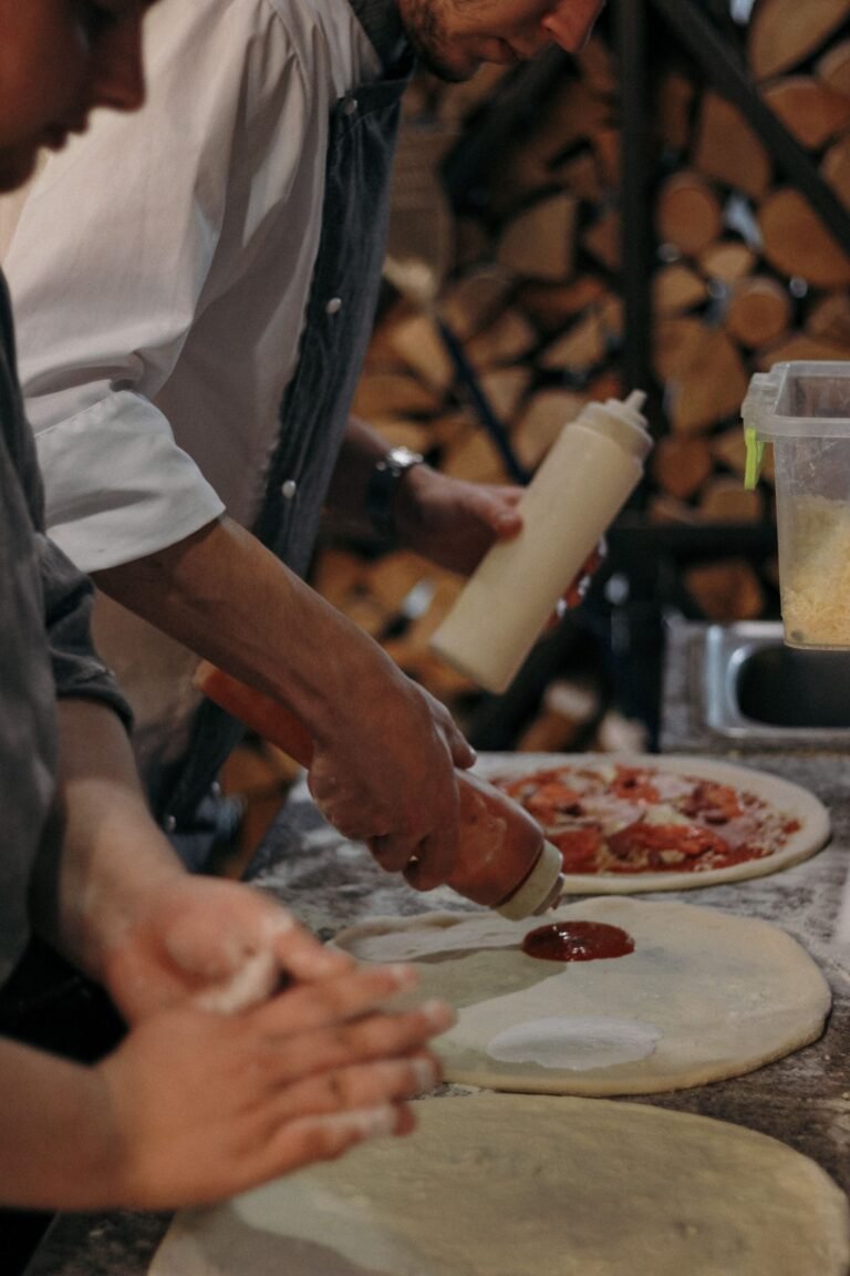 Person Putting Tomato Sauce on a Round Dough