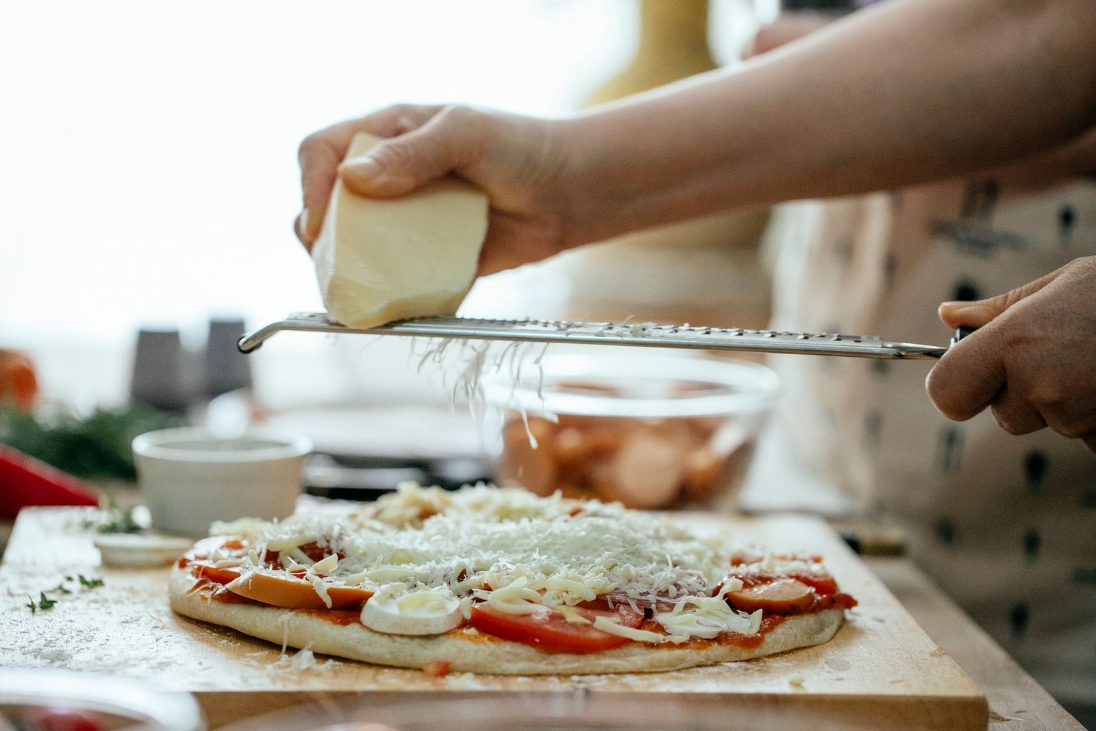 Anonymous person grating cheese on pizza
